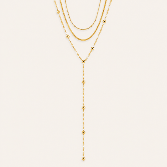 Layered gold Azure Y NECKLACE with a snake chain, a beaded chain and a long ball-bead lariat drop, laid flat on beige.