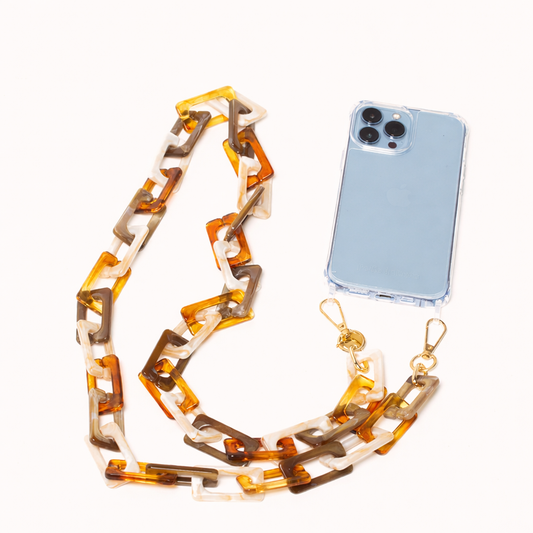 Amber tortoise acrylic chain-link Bennie long phone chain laid beside a clear case phone.