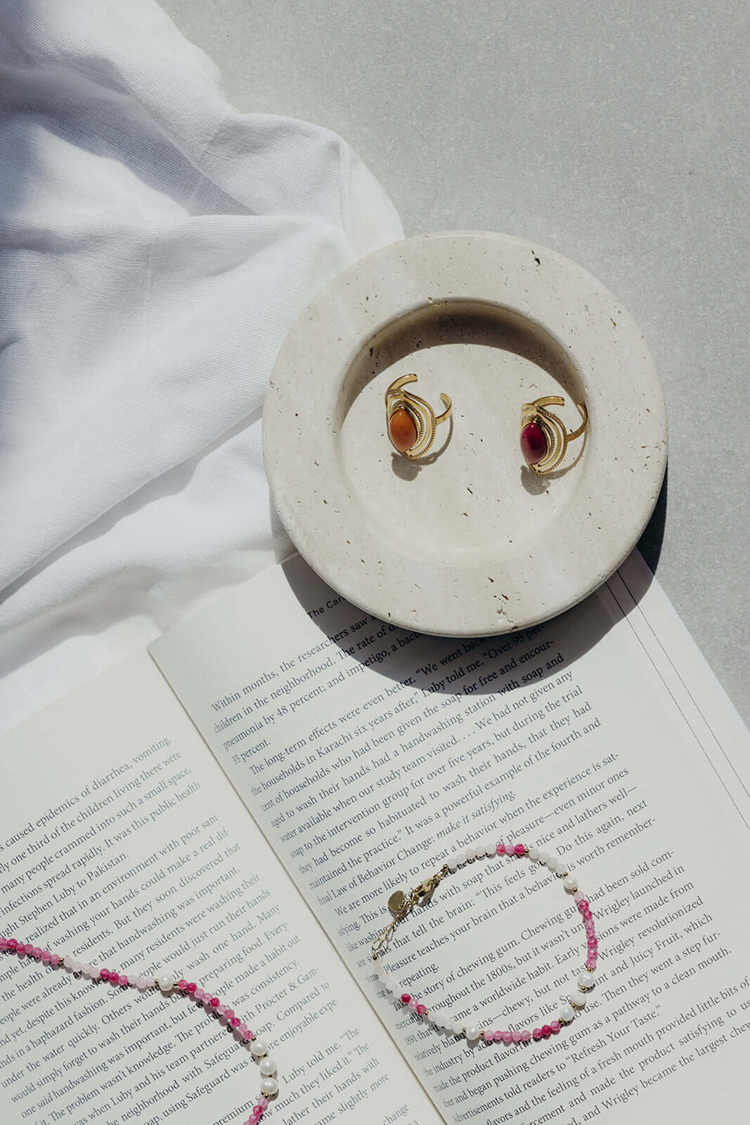 Bianca BRACELET beaded necklace styled on a ceramic dish with gold rings, resting on an open book.