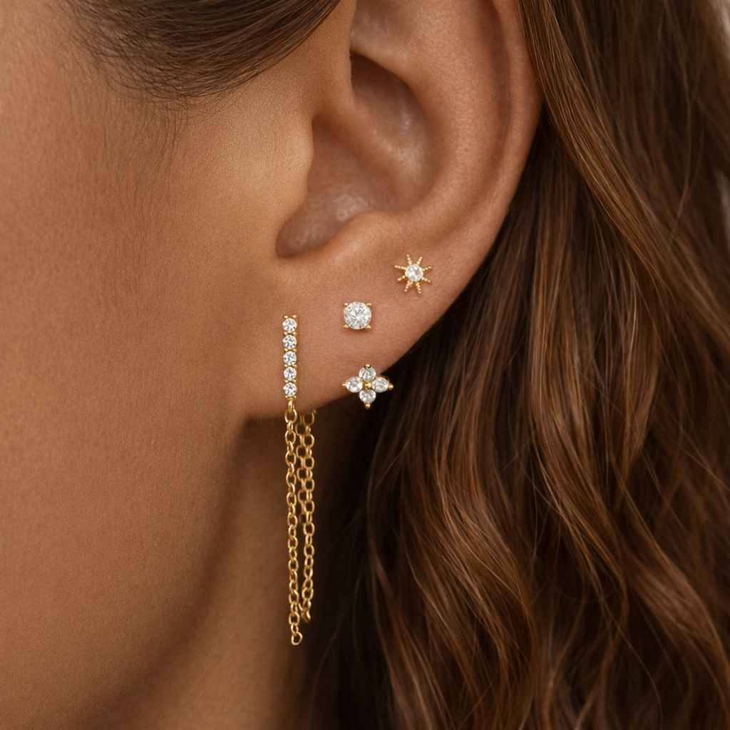 Bianca Set worn on the ear, stacking a star stud, round stud, flower drop, and chain-draped crystal bar along the lobe.