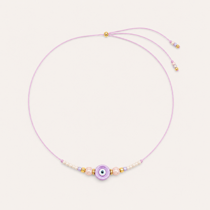 Purple cord Big Eye NECKLACE with beaded pearl and glass accents around a lilac enamel evil eye charm, laid flat.