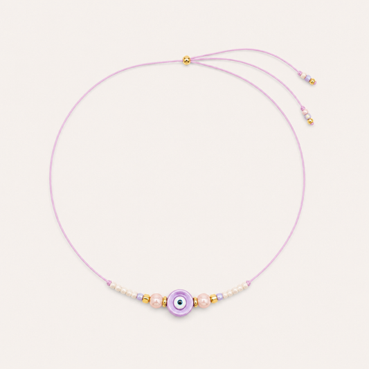 Purple cord Big Eye NECKLACE with beaded pearl and glass accents around a lilac enamel evil eye charm, laid flat.