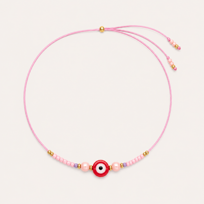 Pink cord Big Eye NECKLACE with beaded pearl and lilac accents around a red enamel evil eye charm, laid flat.