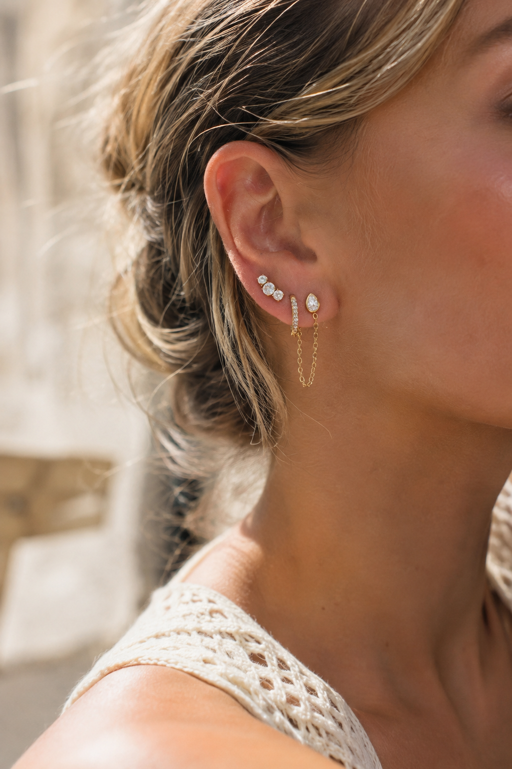 Model wears the Folie à Trois Bijou SET stacked along her ear, mixing zirconia studs, a pavé hoop and a chain-drop earring.
