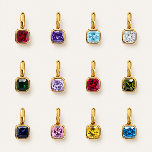 The Birthstone Charm BUNDLE in a flat lay grid, twelve gold-set square birthstone charms in every month's color on cream fabric.