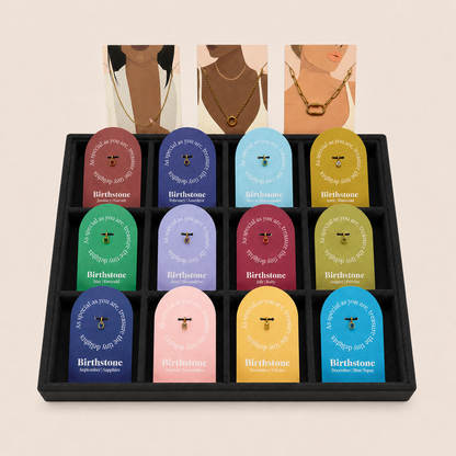 The Birthstone Charm BUNDLE in a black tray of twelve Birthstone gift tags with three illustrated lifestyle cards propped above.
