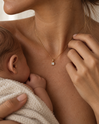 A mother breastfeeds her newborn while wearing the Folie à Trois Birthstone Charm BUNDLE's clear-stone square charm on a fine gold chain.