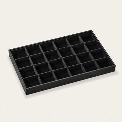 Black jewelry tray display lined with small square velvet compartments for organizing stud earrings and rings.