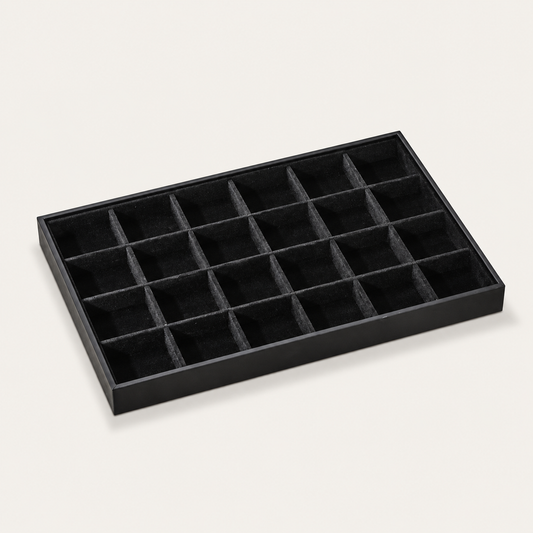 Black jewelry tray display lined with small square velvet compartments for organizing stud earrings and rings.