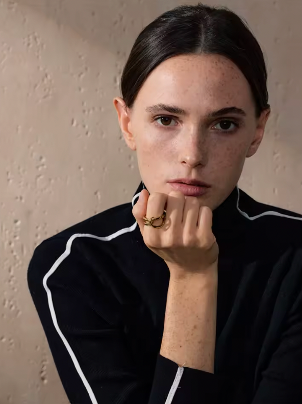 Model rests her chin on a hand wearing the gold Blaze RING, dressed in a black top with white piping.