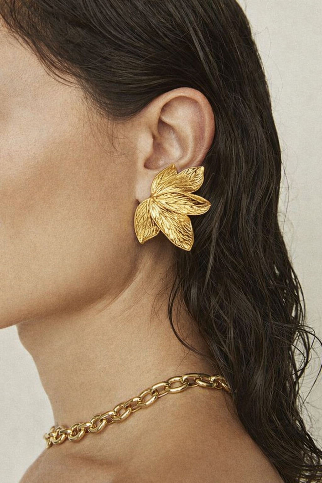 Bloom Earring worn on the ear in gold, the textured petal design framing the lobe beside a chain necklace.