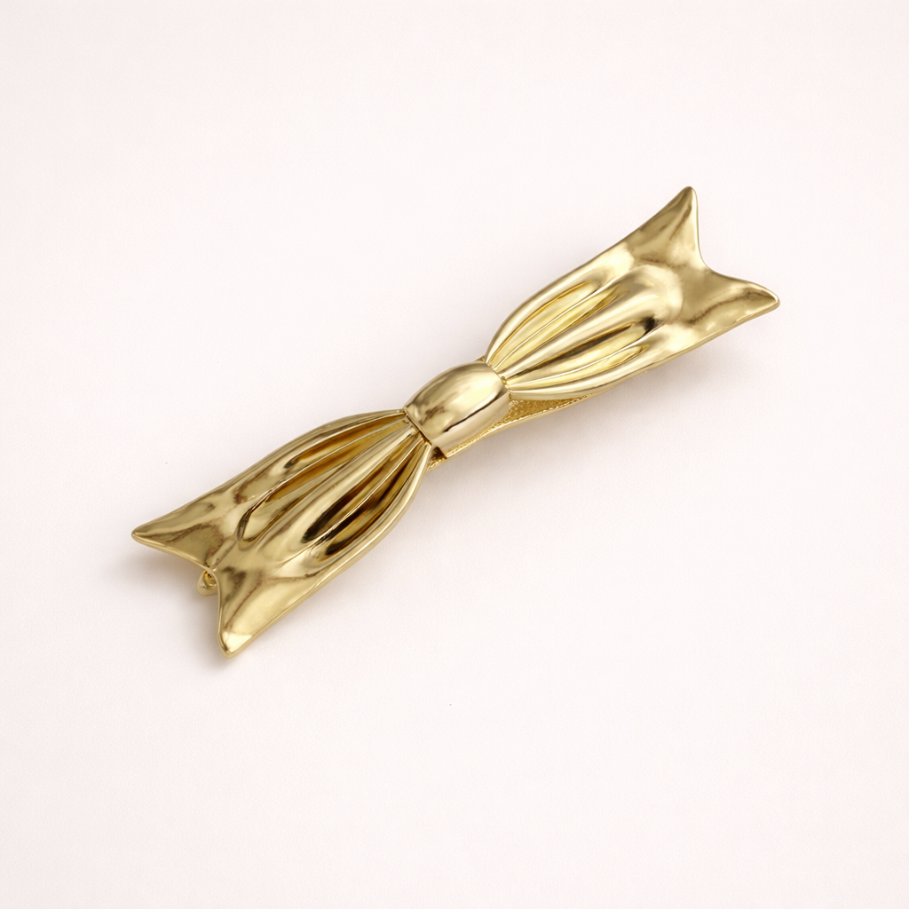 Bow HAIR CLIP sculptural gold-tone metal barrette shaped like a bow, studio shot.