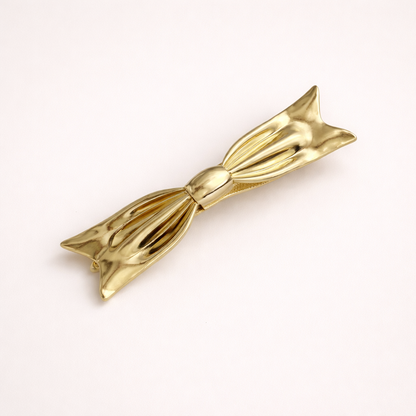 Bow HAIR CLIP sculptural gold-tone metal barrette shaped like a bow, studio shot.