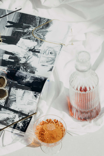 Braided Babe BRACELET styled lifestyle shot of a vintage magazine, gold trinkets and a glass of rose on white linen.