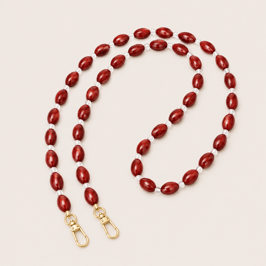 Folie à Trois Bramble long wholesale phone chain in deep red oval beads with clear glass spacers and gold clasps, coiled on a cream background.