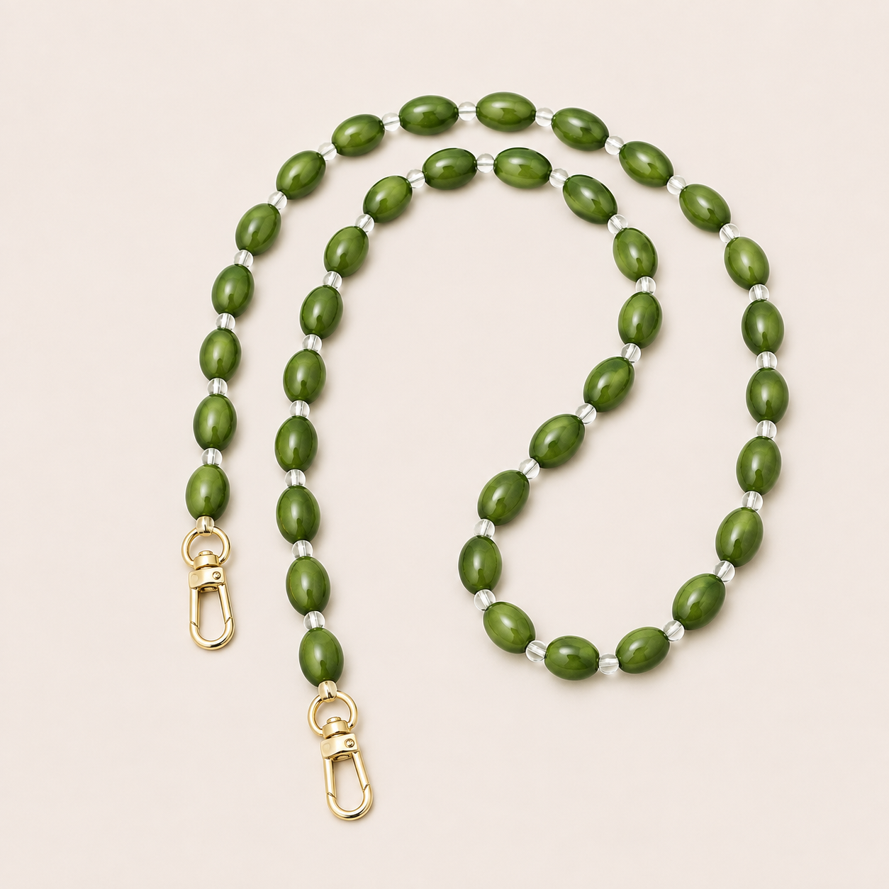 Folie à Trois Bramble long wholesale phone chain in olive green oval beads with clear glass spacers and gold clasps, coiled on a cream background.