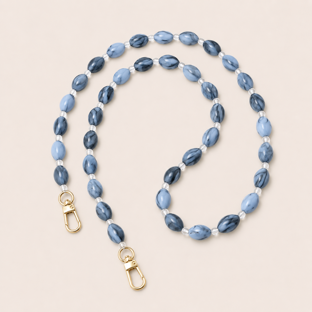 Folie à Trois Bramble long wholesale phone chain in blue marbled oval beads with clear glass spacers and gold clasps, coiled on a cream background.