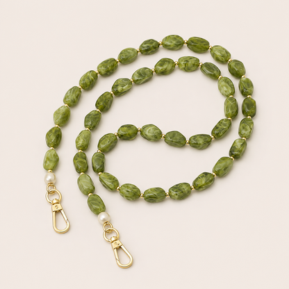 Folie à Trois Briar long wholesale phone chain in green marbled nugget beads with gold spacers, pearl accents and gold clasps, coiled on a cream background.
