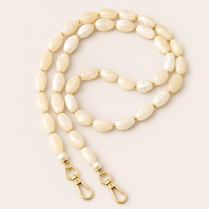Folie à Trois Briar long wholesale phone chain in ivory pearlescent nugget beads with gold spacers, pearl accents and gold clasps, coiled on a cream background.