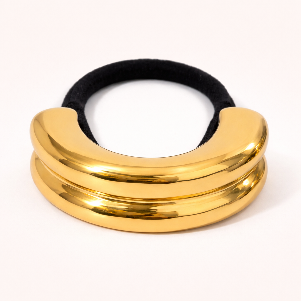 Bridgette Hair Tie double-ridged gold sculptural bead on a black elastic band, studio flat-lay.
