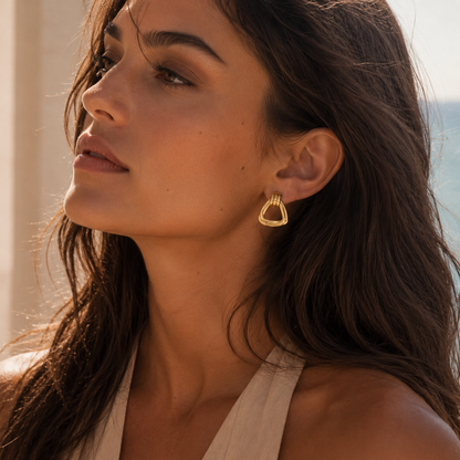 A model wears a gold Brienne EARRINGS hoop with a triangular, open ridged design and a ribbed top detail.