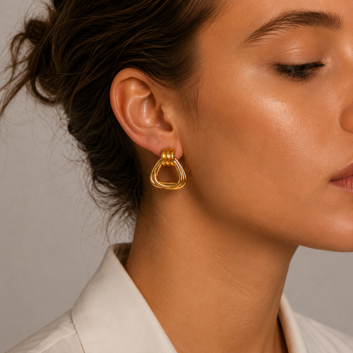 Close-up of a model wearing a gold Brienne EARRINGS hoop with a triangular, open ridged design and a ribbed top detail.