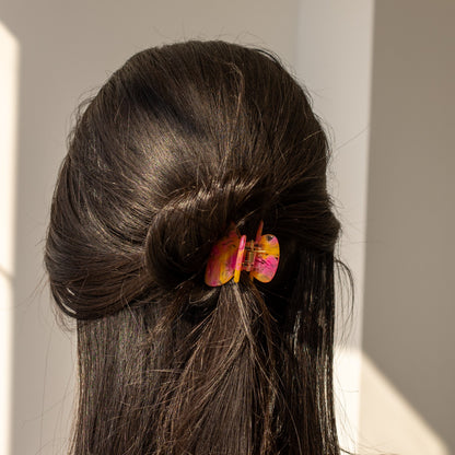 Bubblegum HAIR CLIP in pink and orange, worn holding a twisted bun on dark hair, back view in sunlight.