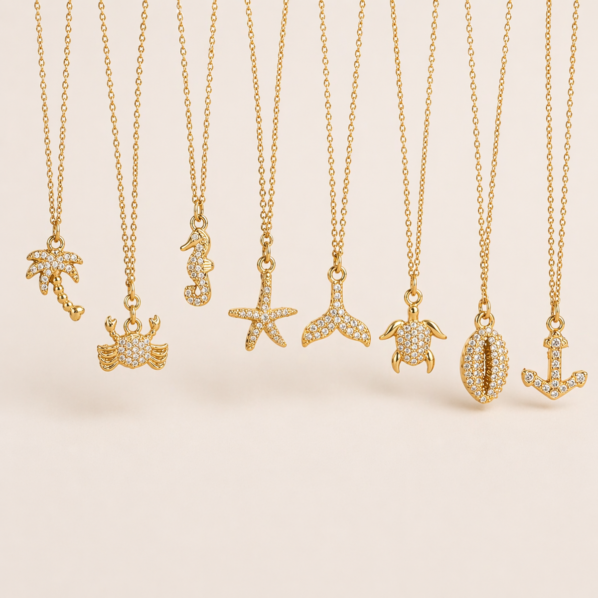 The By The Sea NECKLACE collection, showing eight gold pave charms: palm tree, crab, seahorse, starfish, turtle, cowrie shell, and anchor.