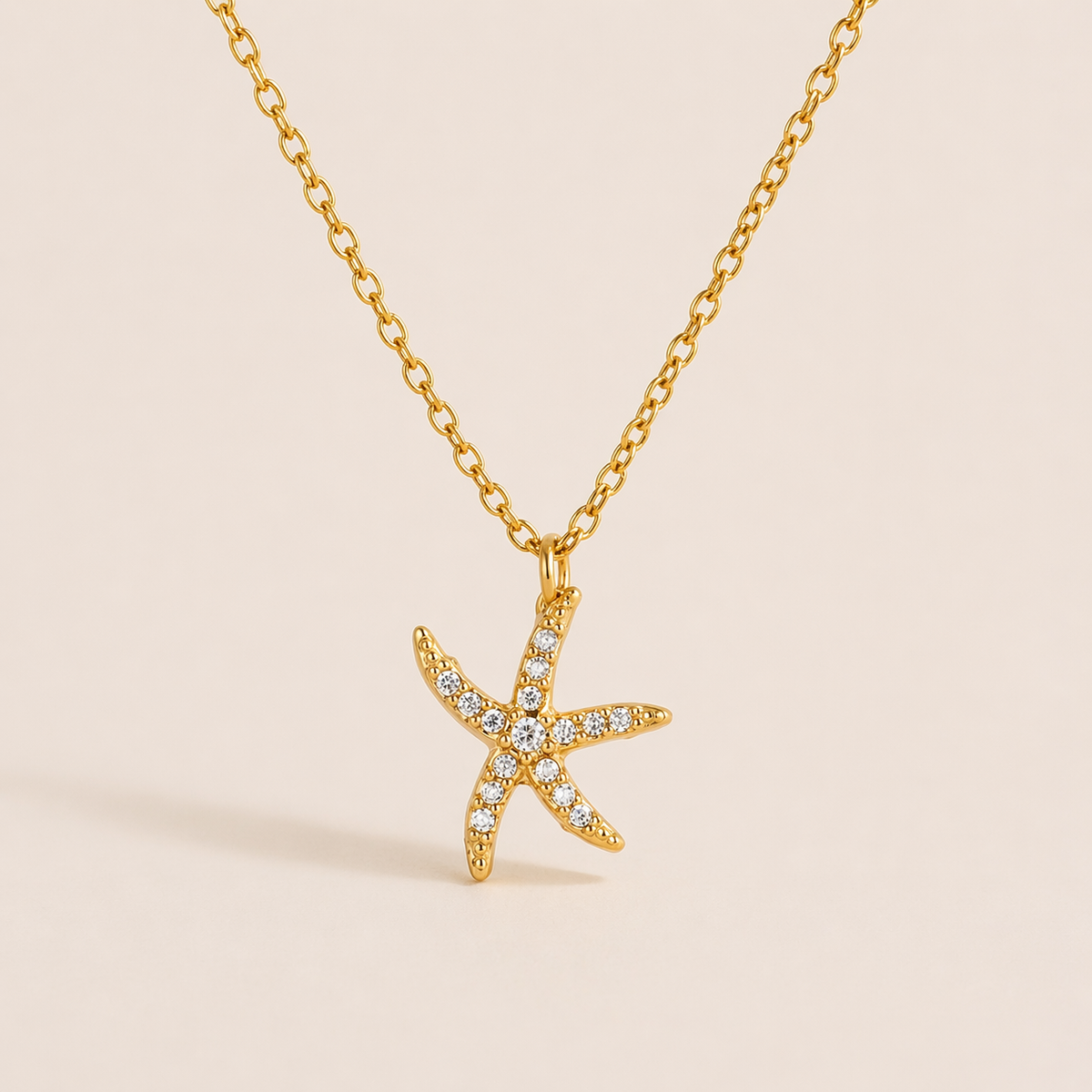 The By The Sea NECKLACE in the pave starfish style, hanging against a plain beige background to show its crystal-set points.