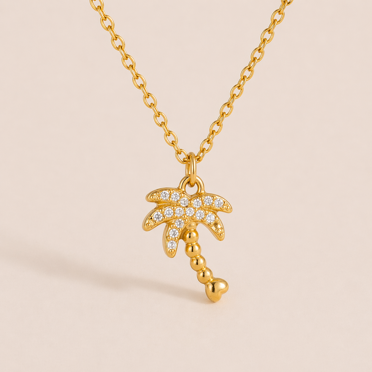 The By The Sea NECKLACE in the pave palm tree style, hanging against a plain beige background with its beaded trunk visible.