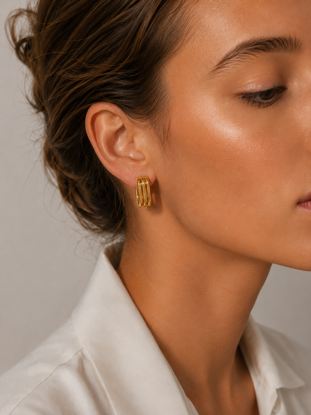 Close-up of a model wearing a gold Cami EARRINGS hoop with multiple stacked ridged bands on her ear.