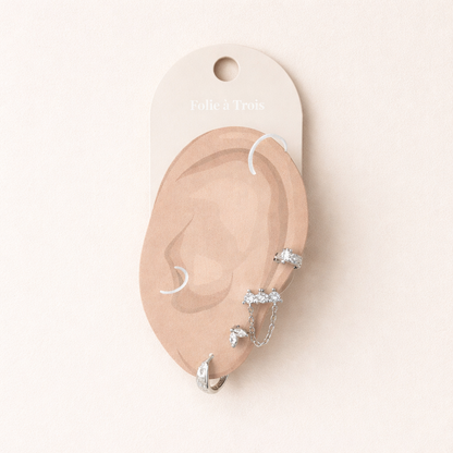 Illustrated Folie a Trois earring card showing the silver-tone Capucine Set pieces on an ear-shaped display.