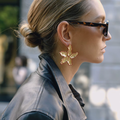A model wears a gold Carrie EARRINGS stud shaped like a textured starfish with a red enamel outline.
