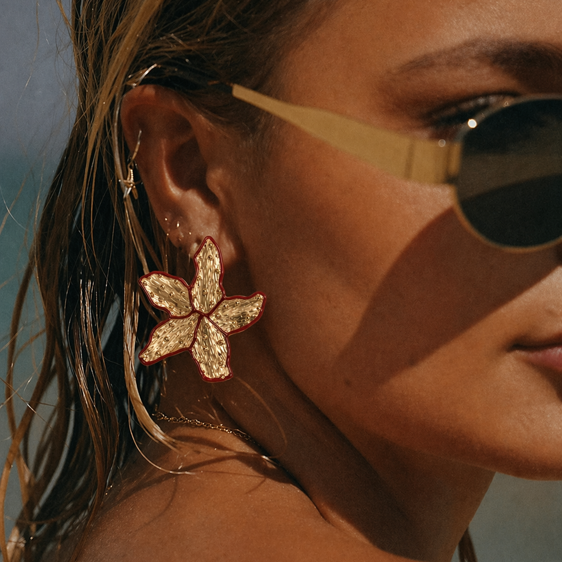 Close-up of a model wearing a gold Carrie EARRINGS stud shaped like a textured starfish with a red enamel outline.