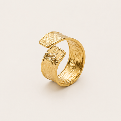 Gold open ring with a wavy, hammered-texture wraparound band, shown in close-up on a cream backdrop — Folie à Trois Cassis RING.