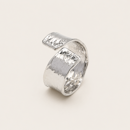 Silver open ring with a wavy, hammered-texture wraparound band, shown in close-up on a cream backdrop — Folie à Trois Cassis RING.
