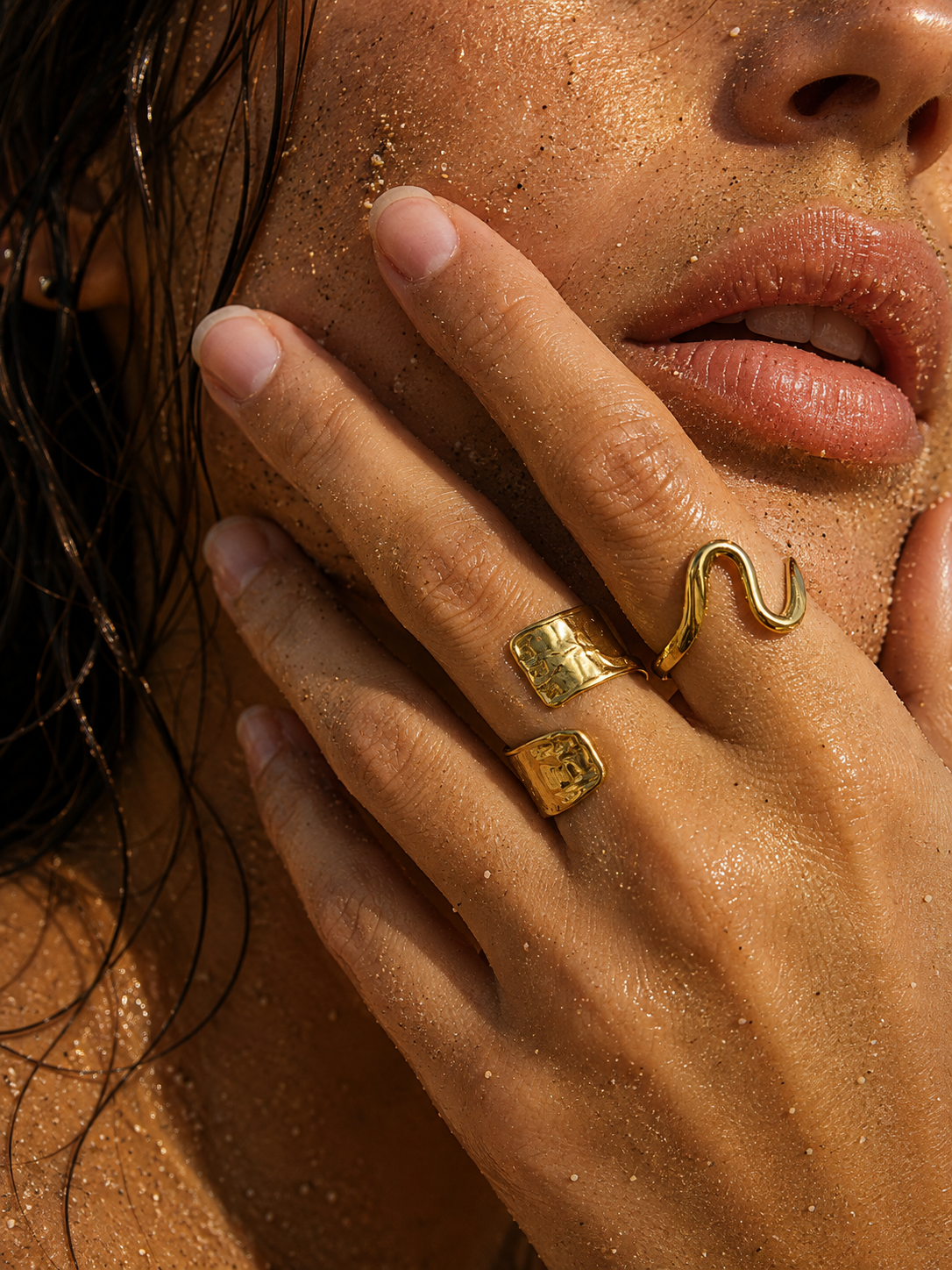 Model wears the gold Cassis RING stacked with the Menton RING on damp, sun-kissed skin, hand raised to her cheek.