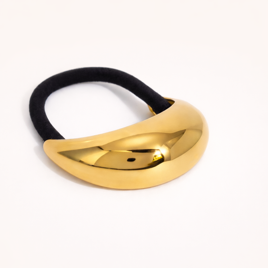 Cecil Hair Tie chunky gold sculptural bead on a black elastic band, studio flat-lay on cream.