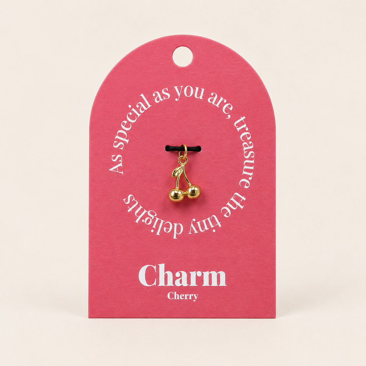 The Cherry CHARM displayed on a coral pink Charm gift tag, the gold cherry pendant hanging from a black cord.
