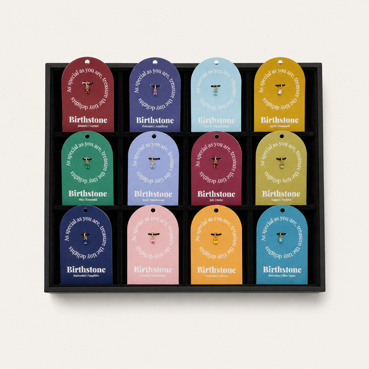 A black tray holding twelve Birthstone gift tags arranged in a 3-by-4 grid, each tag in a different color with a small central animal icon and the brand name Birthstone printed at the bottom.