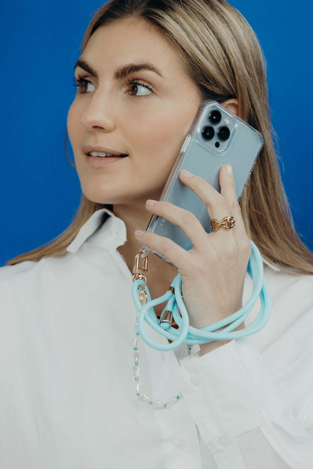 Model against a blue background holds her phone in a clear Classic iPHONE CASE with a mint cord strap attached.