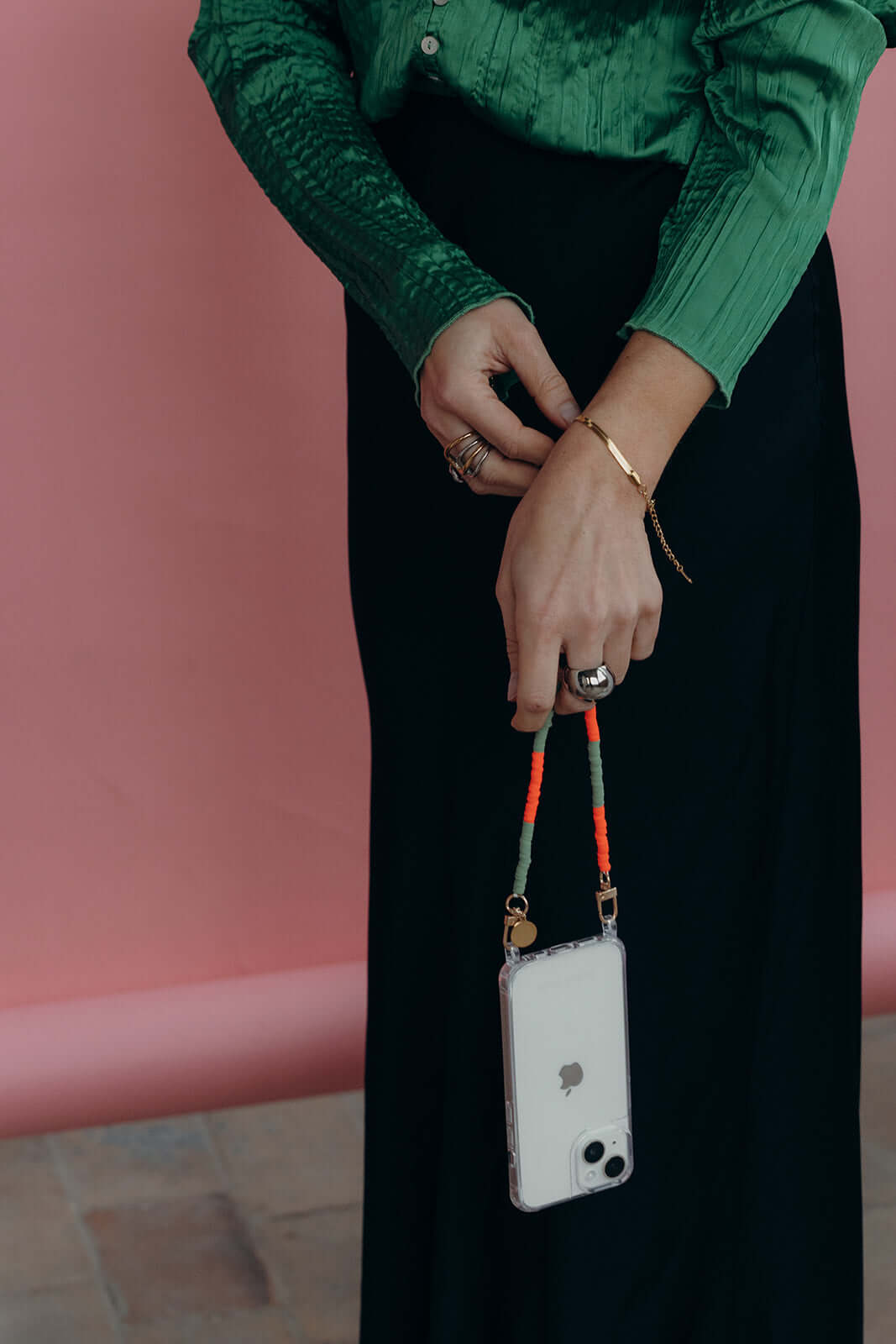 Clear Classic iPHONE CASE with a green and orange beaded cord strap, held by a model in a black skirt and green top.