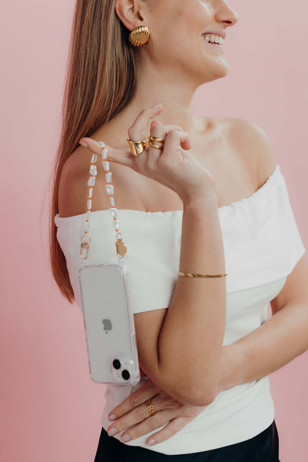 Clear Classic iPHONE CASE with a white pearl beaded strap draped over a model's shoulder, pink background.