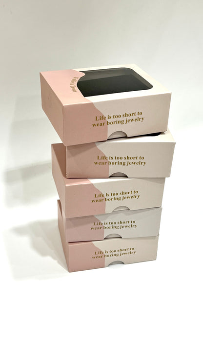 Stack of five pink and cream Folie à Trois clear-window gift boxes with matching gold branding.