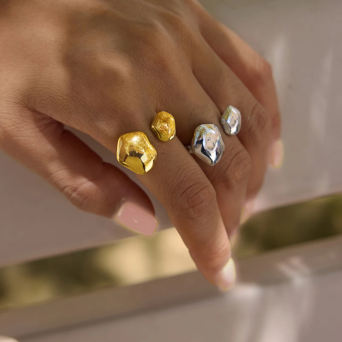 Gold and silver-tone Cloud RINGS on a hand resting on a gold-edged tray, polished organic ends — Folie à Trois