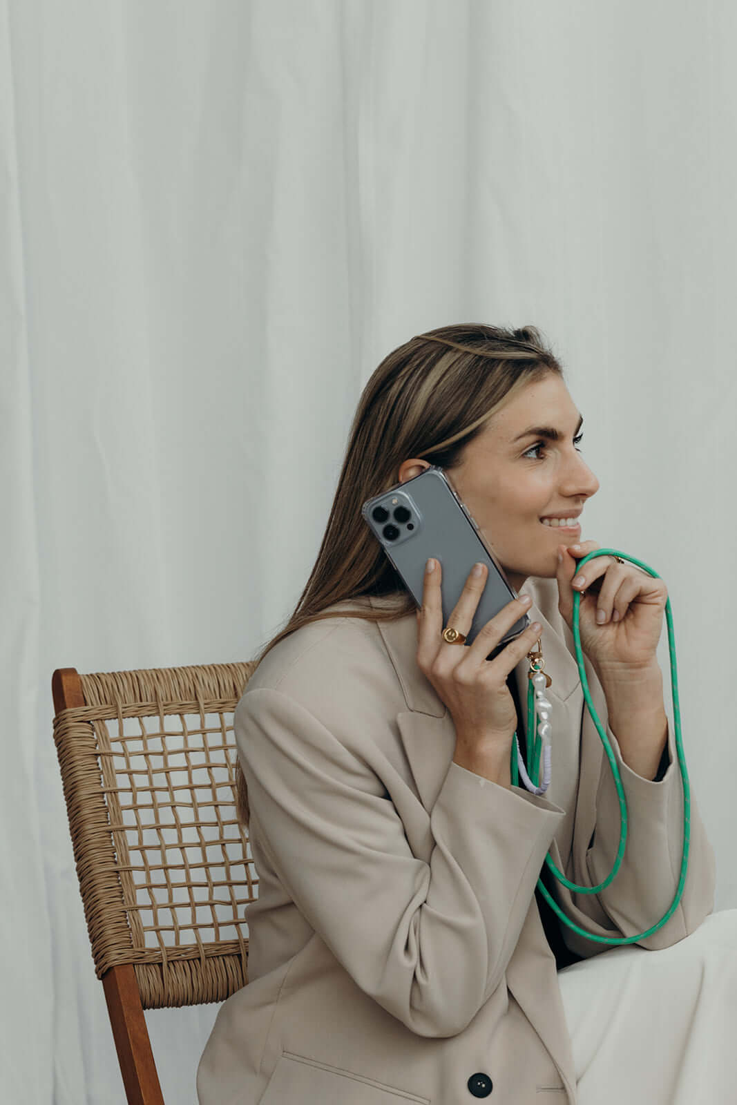 Sage green Colorful PHONE CORD worn by a model on a phone call, seated in a wicker chair.