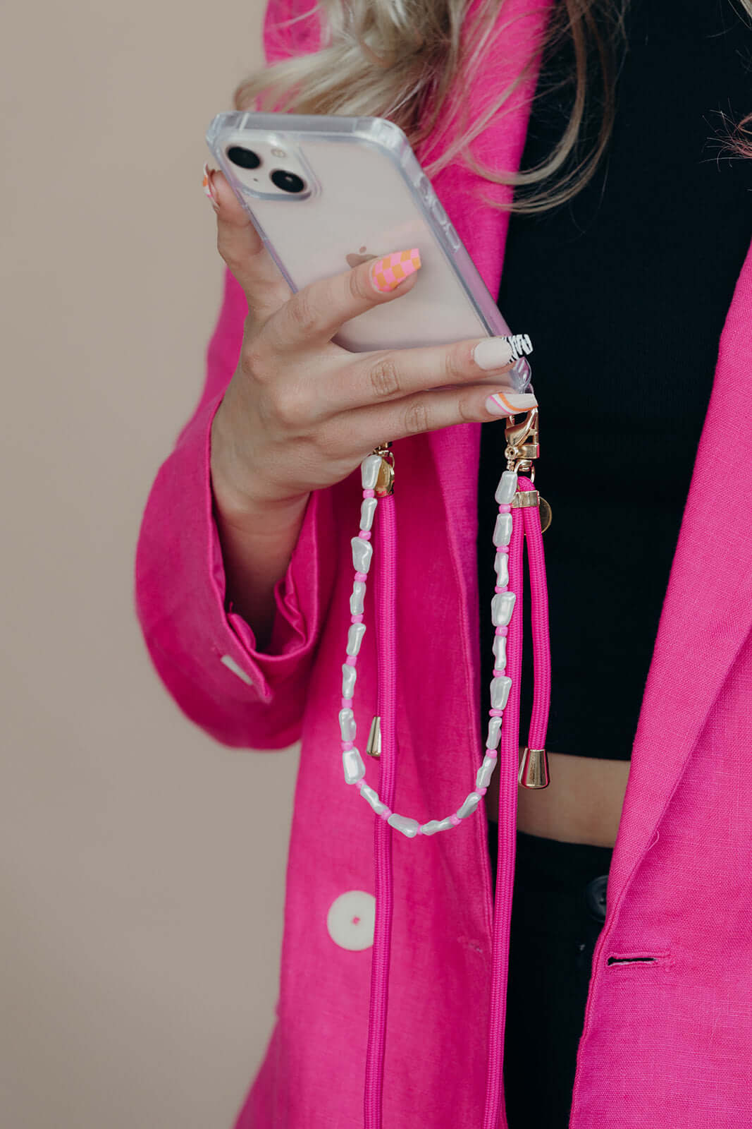 Pink and white beaded phone strap held by a model wearing a hot pink blazer, close-up shot.