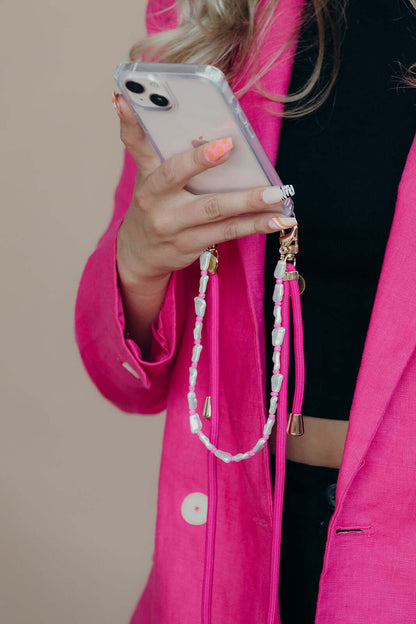 Pink and white beaded phone strap held by a model wearing a hot pink blazer, close-up shot.