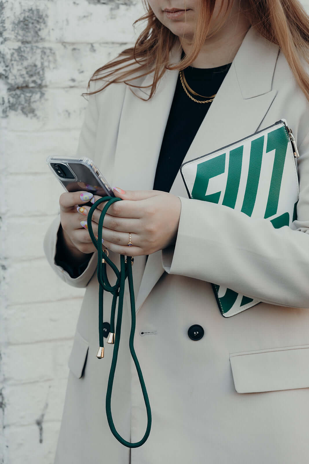 Dark green Colorful PHONE CORD, model holding her phone beside a green striped clutch bag.