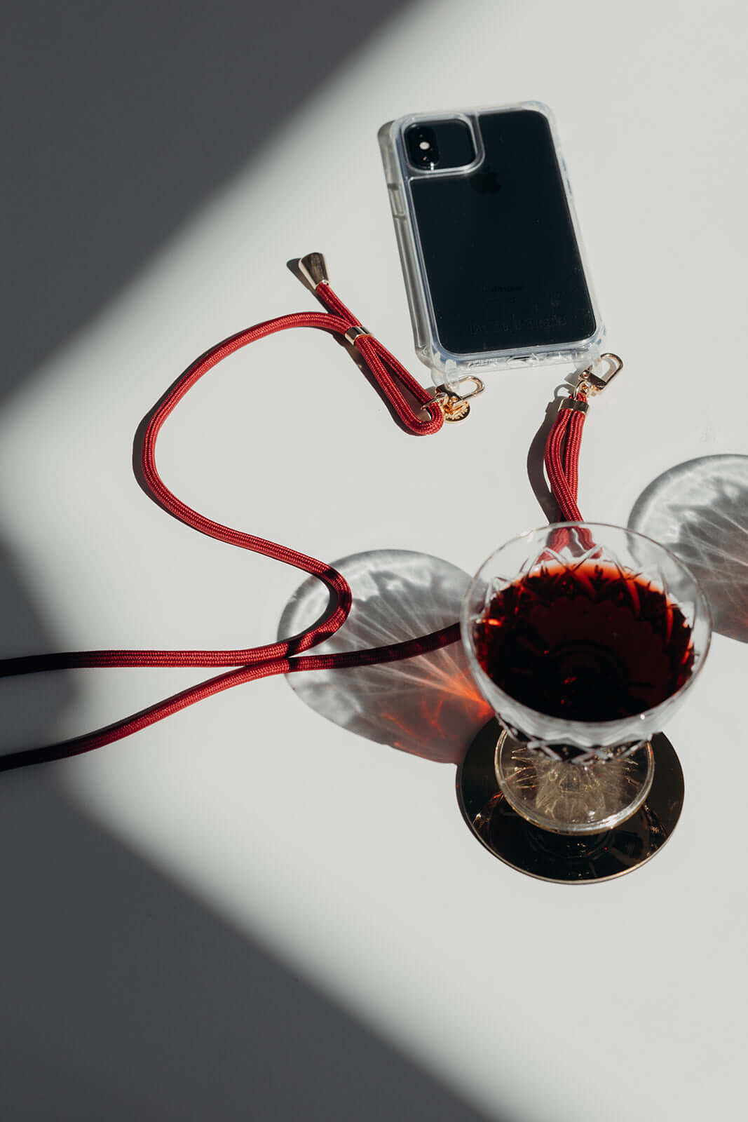 Dark red Colorful PHONE CORD, phone resting beside a glass of red wine on a sunlit table.